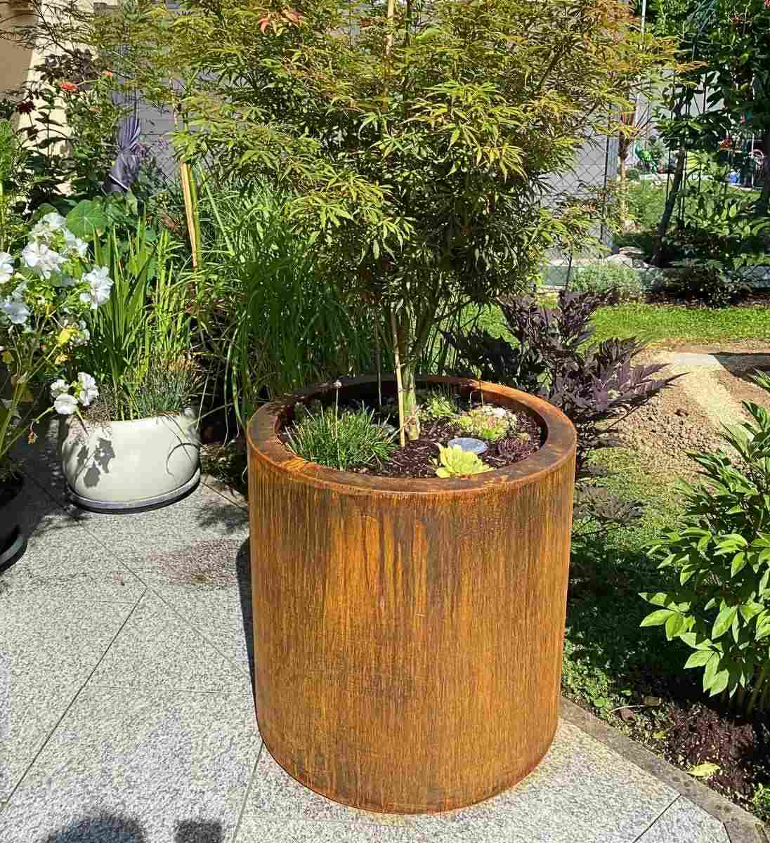 Runder Pflanzkübel im Gartenbeet mit natürlicher Bepflanzung aus Cortenstahl