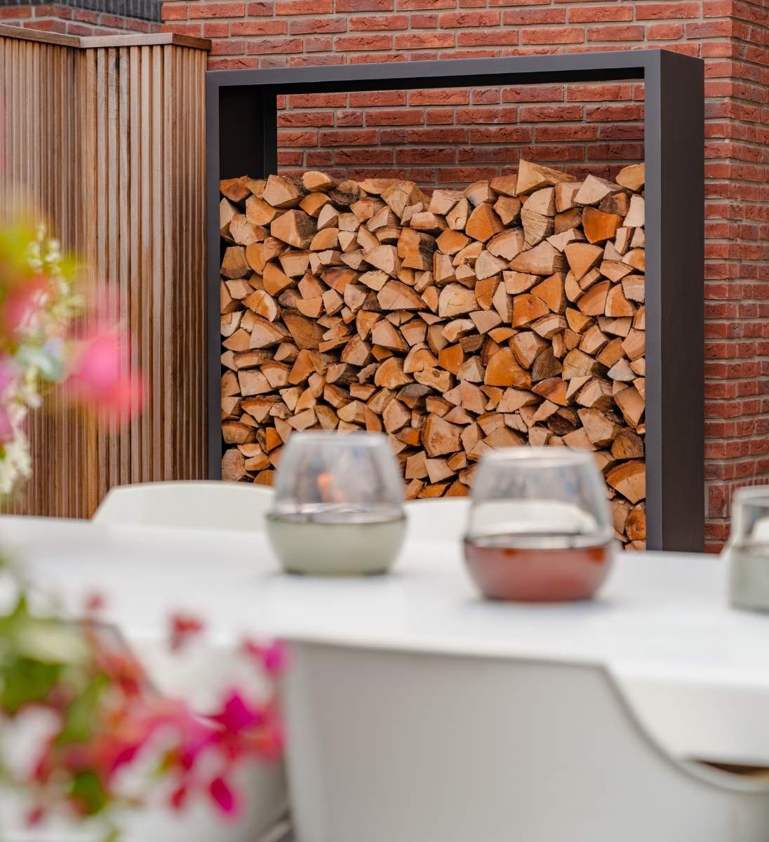 Holzlager Metall Schwarz 60x40x180 cm auf Terrasse, dekorativ befüllt mit Brennhol
