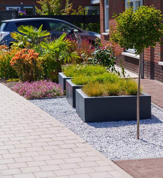 Anthrazitfarbene Fiberglas-Pflanzkübel im Vorgarten mit Gras bepflanzt